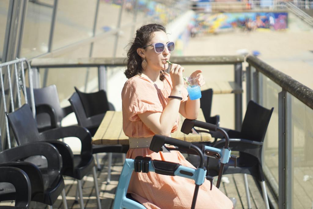 woman in a dress sitting on a rollator walking aid on a restaurant-terrace